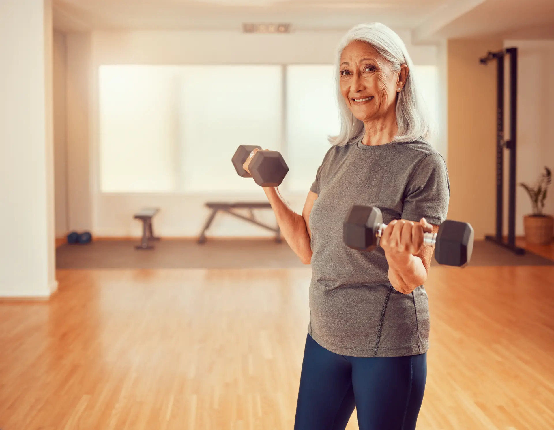 Older woman holding dumbbells in a gym.