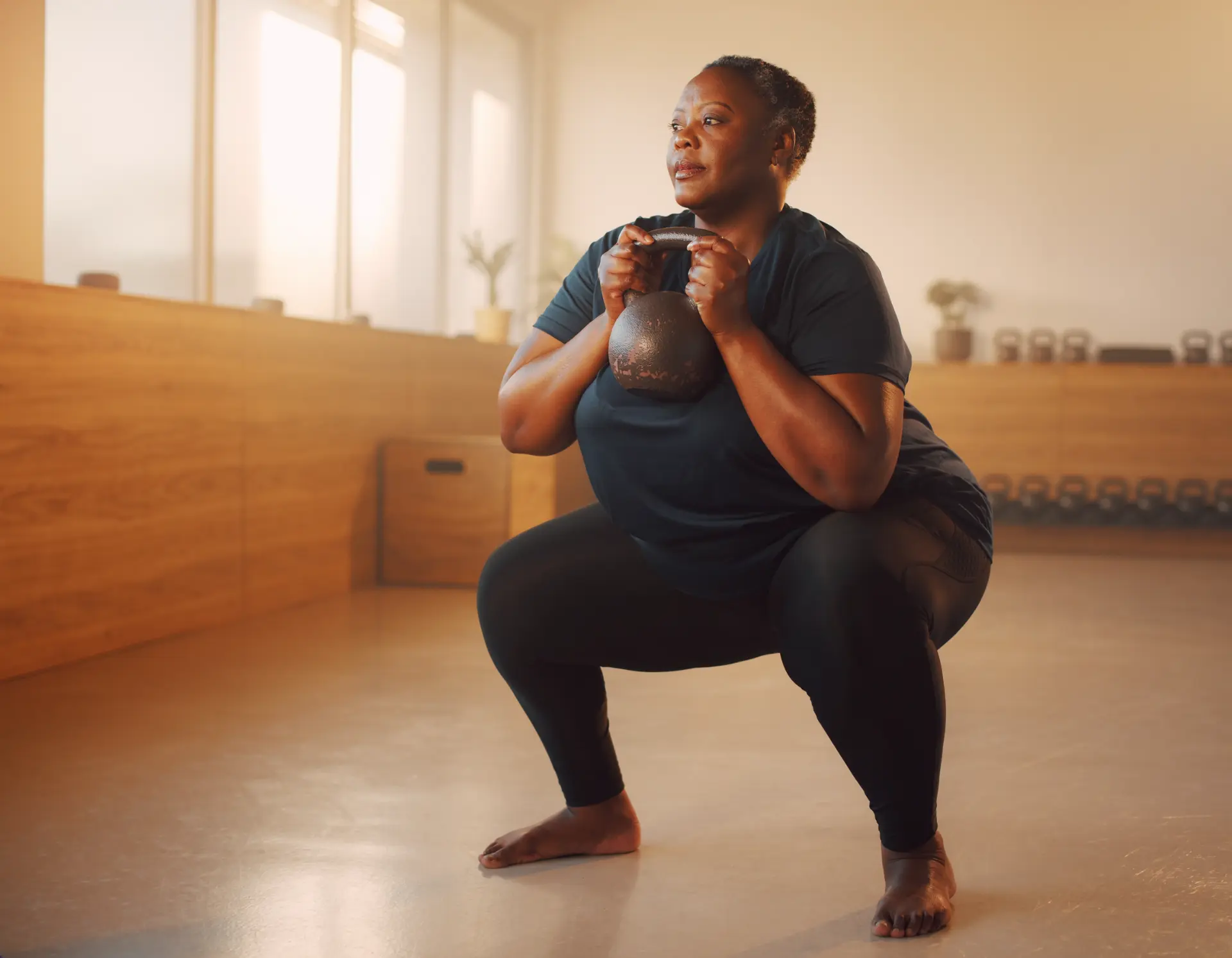 Woman performing a kettlebell squat in a bright studio.