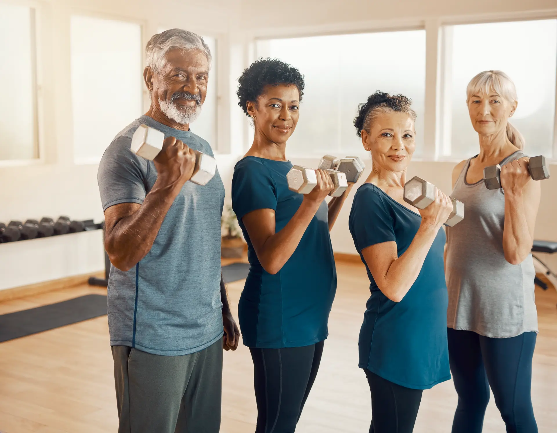 Four older adults holding dumbbells in a bright training space.